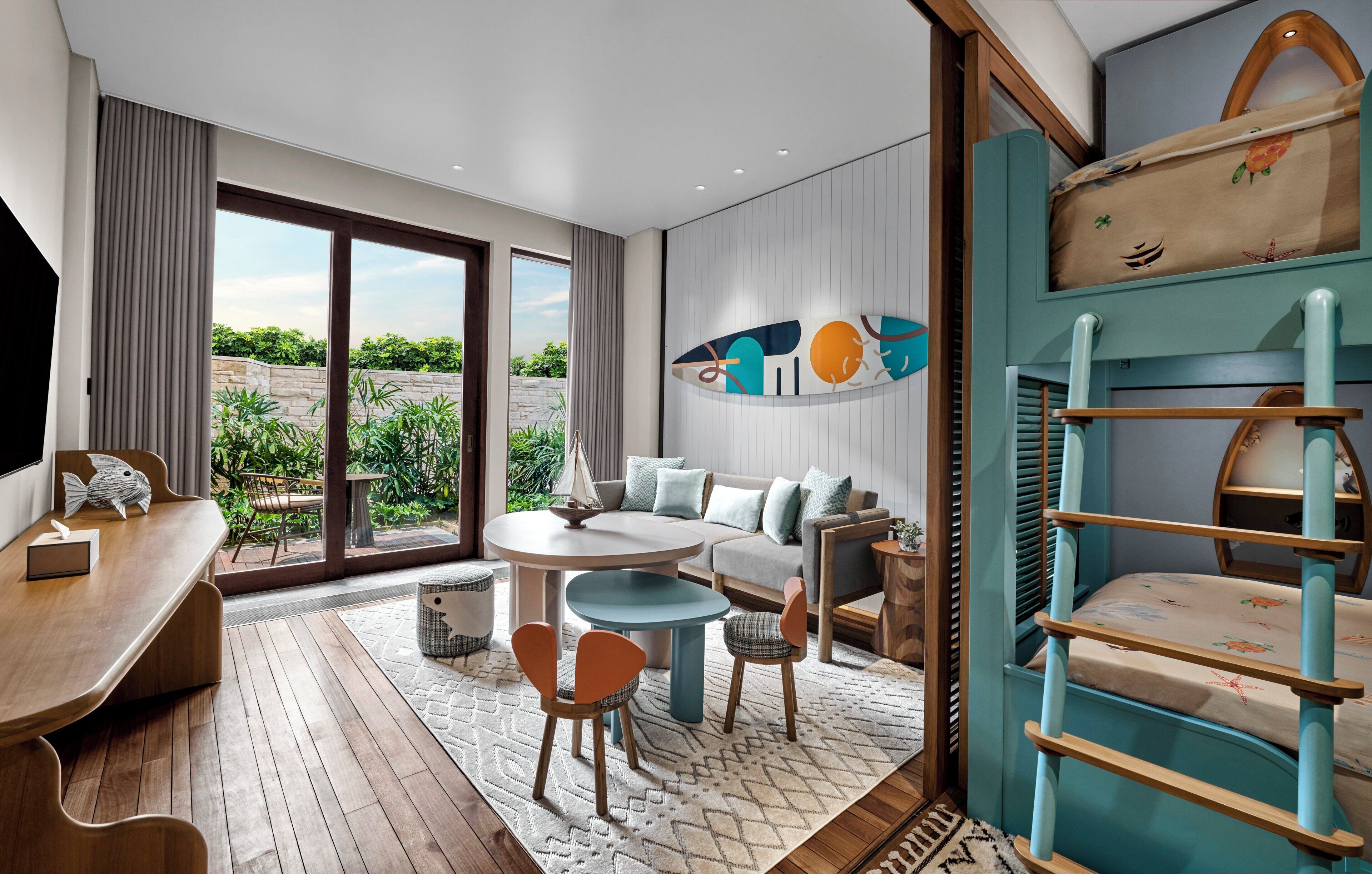 A modern room with a dining area, a sofa set, a children's bunk bed, and a large window offering a view of greenery.
