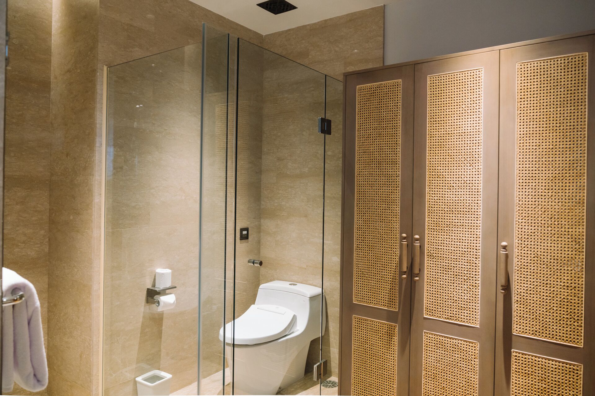A modern bathroom with a glass-enclosed shower, a toilet, and a walk-in closet with woven doors.