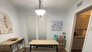 A compact living space with a dining table, benches, a small kitchen area, and a ceiling light fixture. - Cozy 2BR 2BA apt close to Siegen & Womans (Baton Rouge)