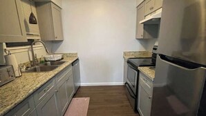 A narrow kitchen with light gray cabinets, a stainless steel refrigerator, and a granite countertop. - Cozy 2BR 2BA apt close to Siegen & Womans (Baton Rouge)