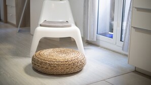 Una silla blanca con cojín y un otomano redondo tejido sobre un suelo de tonos claros.