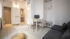 Una sala de estar moderna con un sofá, una mesa de comedor con sillas, un televisor y un estante pequeño.