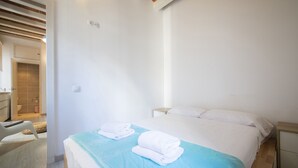 Una habitación de hotel con una cama, dos almohadas, una colcha azul y una mesita de noche blanca.