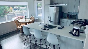 A modern kitchen with a central island, bar stools, a stainless steel refrigerator, and a coffee maker. - Westcoast paradise beside the sea

 (Nanoose Bay)