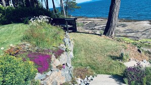 A garden with a bench overlooking a body of water. - Westcoast paradise beside the sea

 (Nanoose Bay)