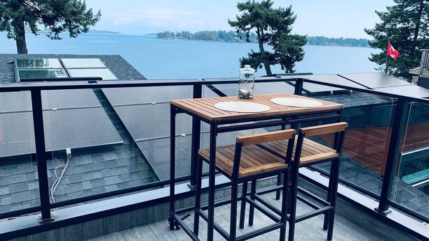 A balcony with a wooden table and chair, overlooking a body of water and trees. - Westcoast paradise beside the sea

 (Nanoose Bay)