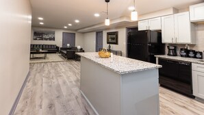 A modern kitchen with a granite countertop, black appliances, and a dining area with a sofa and table. - ✧KC Speedway Retreat - 10 mins to Everything!✧ (Kansas City)