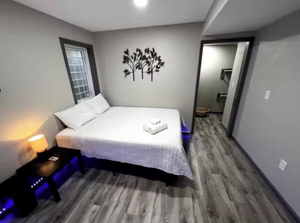 Un dormitorio con cama, mesita de noche, un adorno en la pared y una puerta que da a otra habitación.