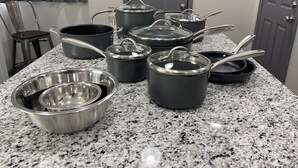 A kitchen counter with various pots and pans, a chair, and a door in the background. - ✧KC Speedway Retreat - 10 mins to Everything!✧ (Kansas City)