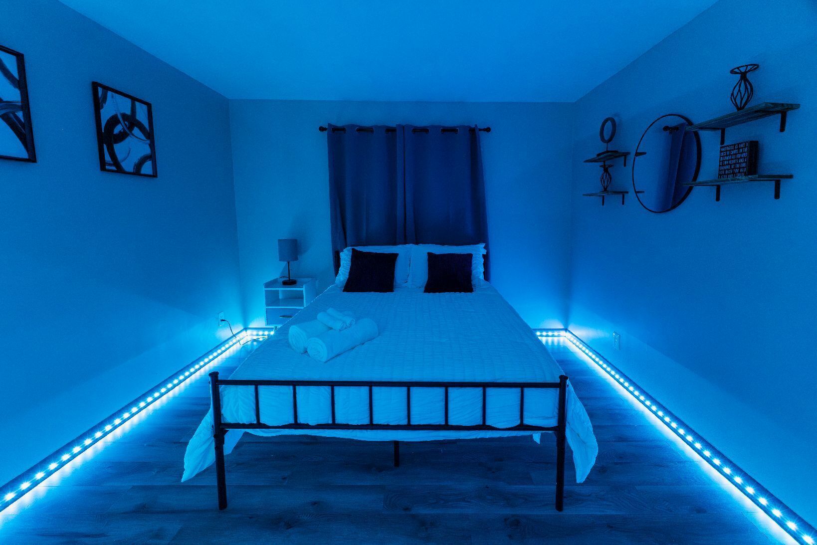 A bedroom with a bed, curtains, a bedside table, and wall-mounted shelves.