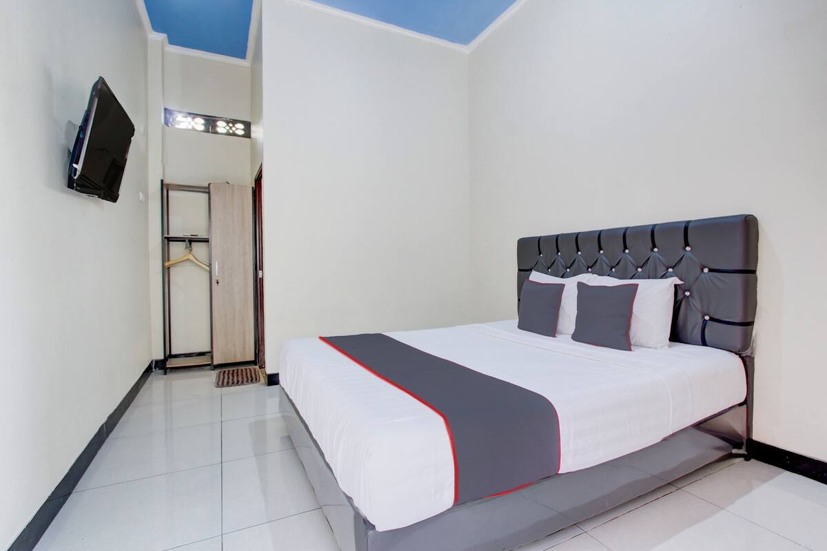 Une chambre d’hôtel avec un lit, un téléviseur fixé au mur et une porte donnant sur un couloir.