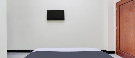 Una habitación con una cama, una puerta de madera y un objeto negro pequeño en la pared.