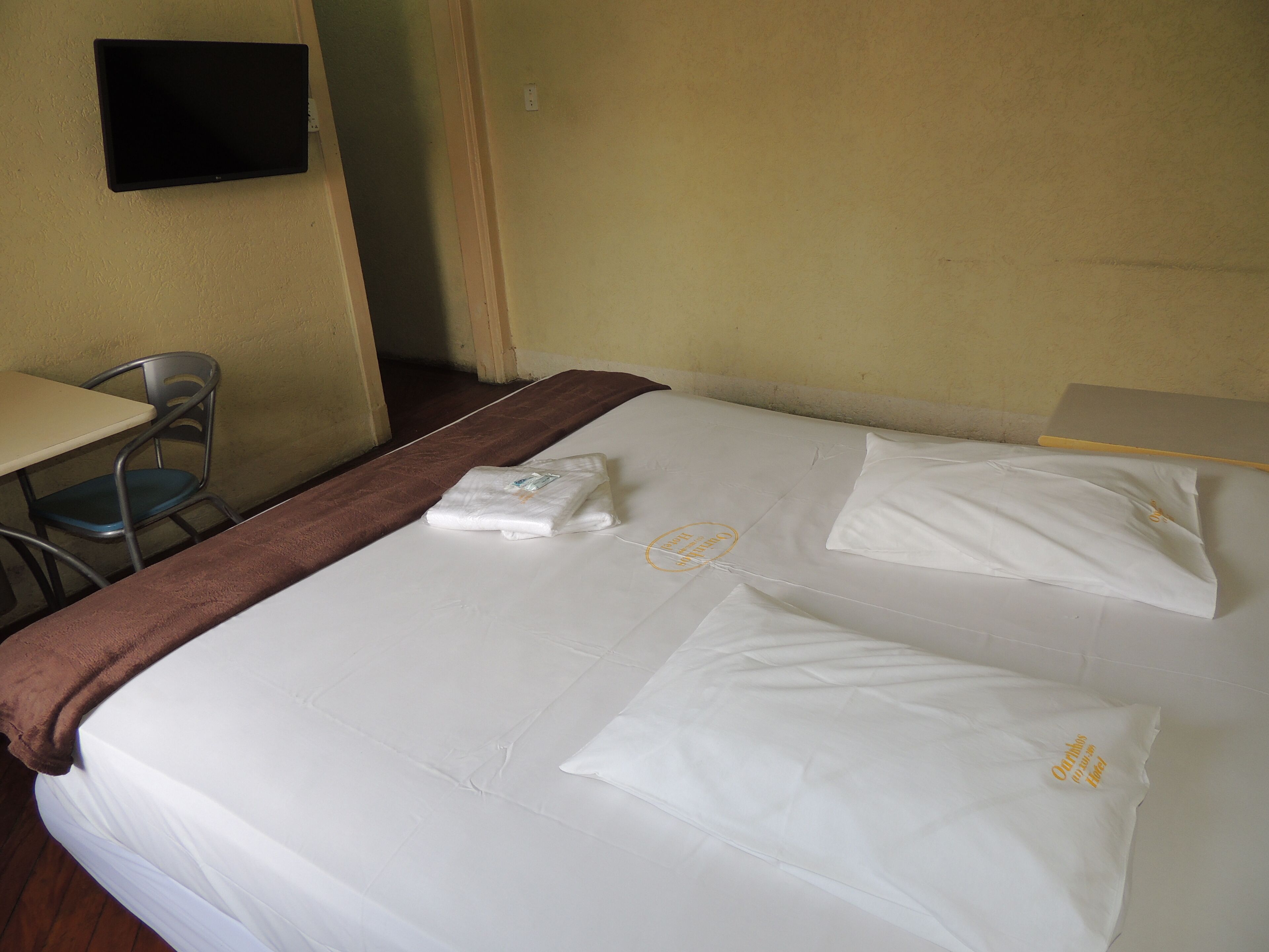 Une chambre d’hôtel avec un lit, une chaise, un bureau et un téléviseur fixé au mur.
