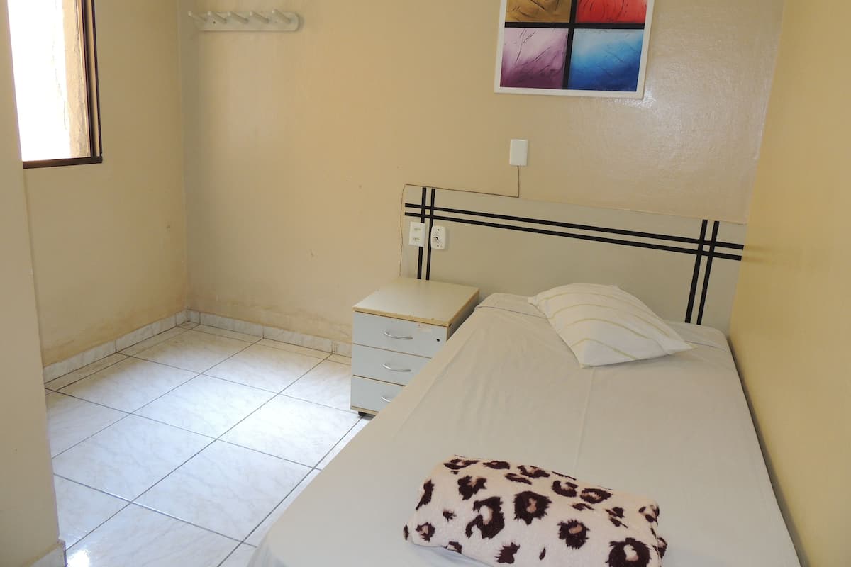 A small, clean room with a bed, a nightstand, and a wall-mounted shelf.