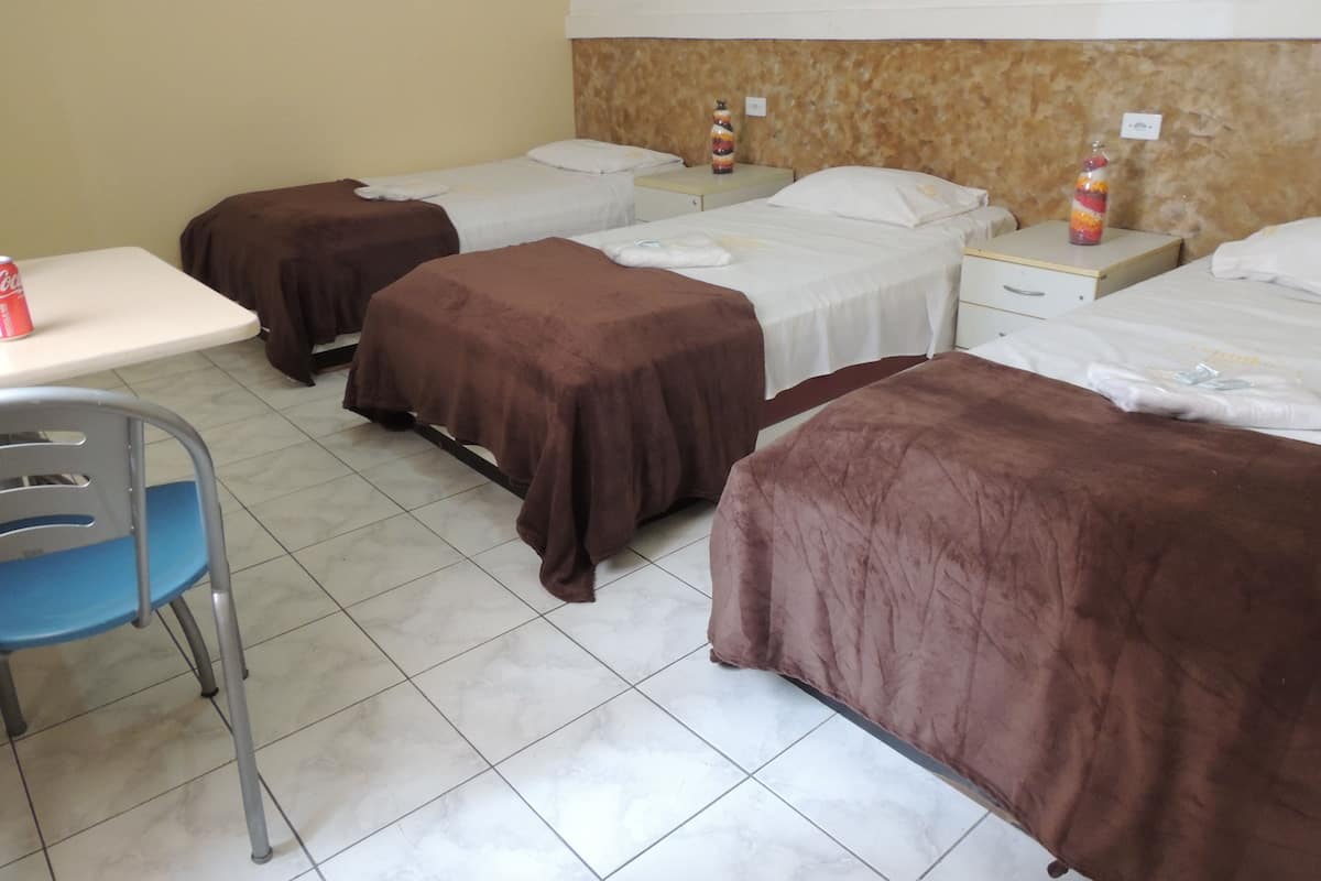 A hotel room with four beds, a small table, and a chair.