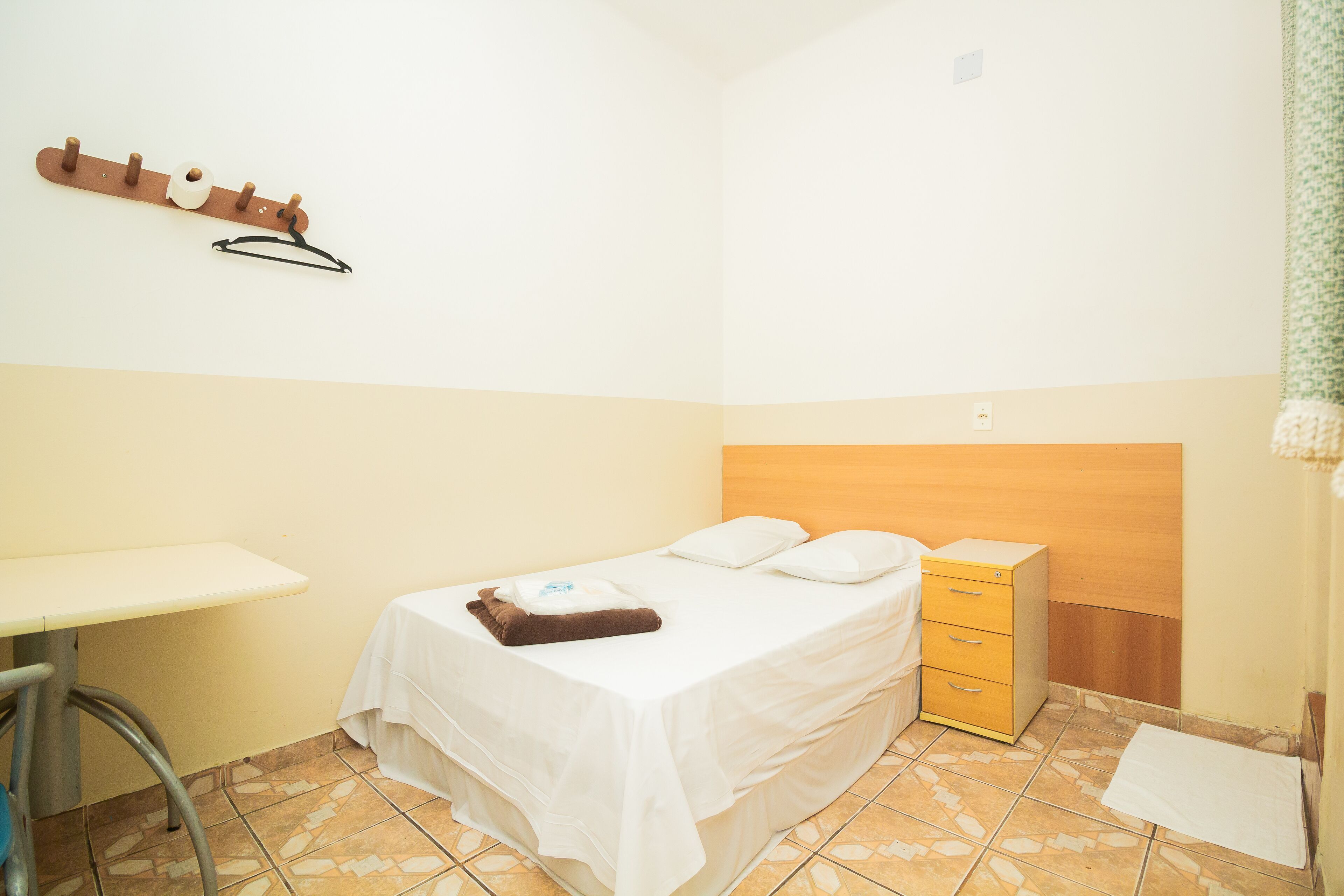 Una habitación pequeña y limpia con una cama, un escritorio y una mesita de noche de madera.