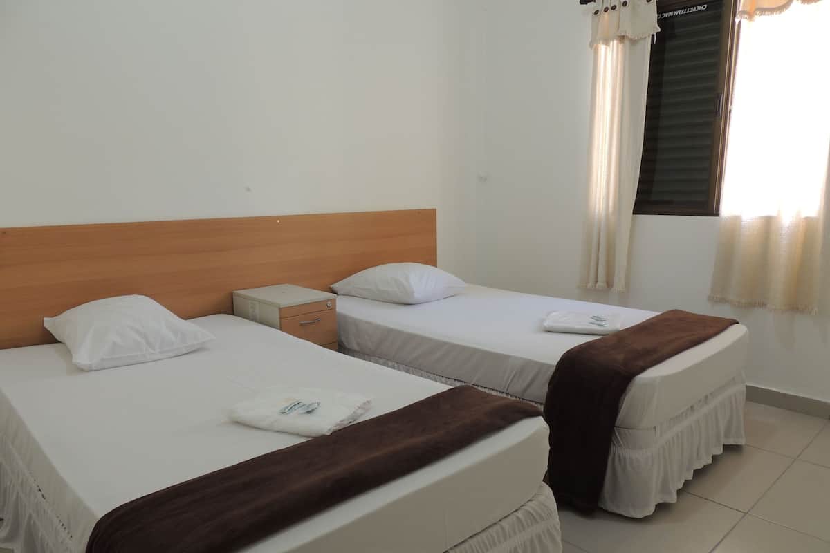 A hotel room with two beds, a wooden headboard, a nightstand, and a window with curtains.