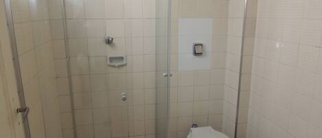 Une petite salle de bain carrelée, équipée de toilettes, d’une douche et d’une poubelle.