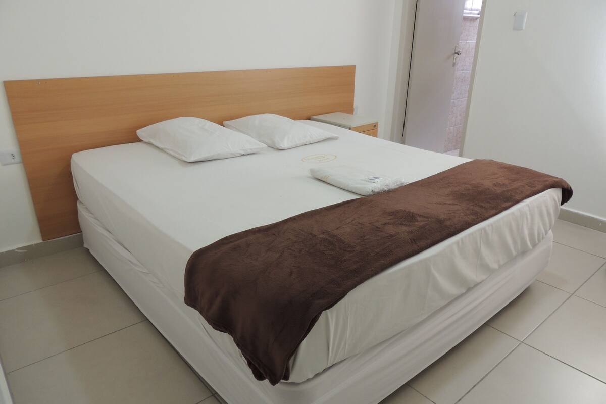 A bed with a wooden headboard, white bedding, and a brown blanket.