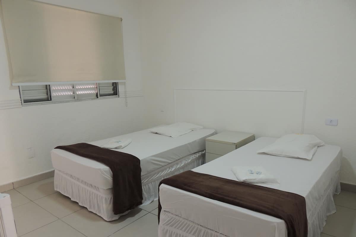 A hotel room with two single beds, a small bedside table, a nightstand, and a large mirror above the beds.
