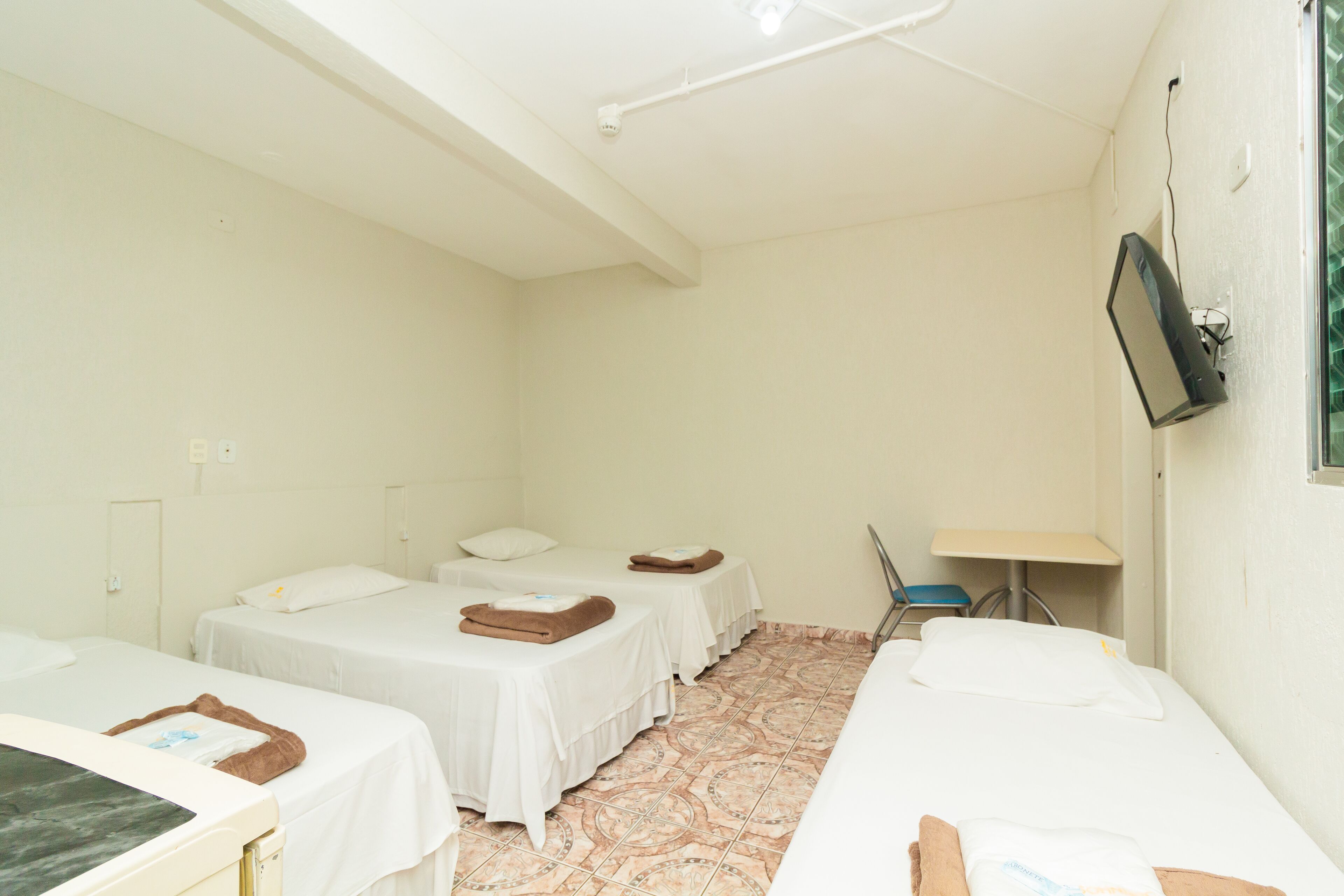 Une chambre d’hôtel avec deux lits simples, un bureau, une chaise et un téléviseur fixé au mur.