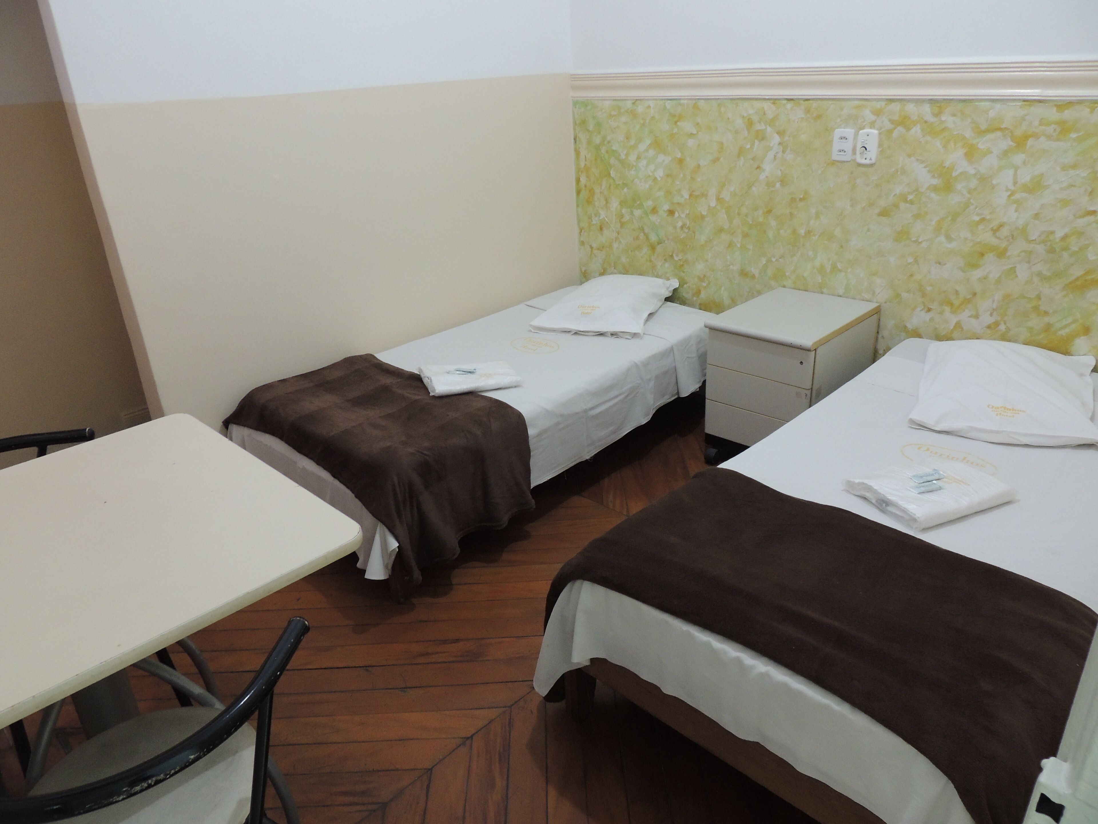 A hotel room with two single beds, a small table, and a chair.