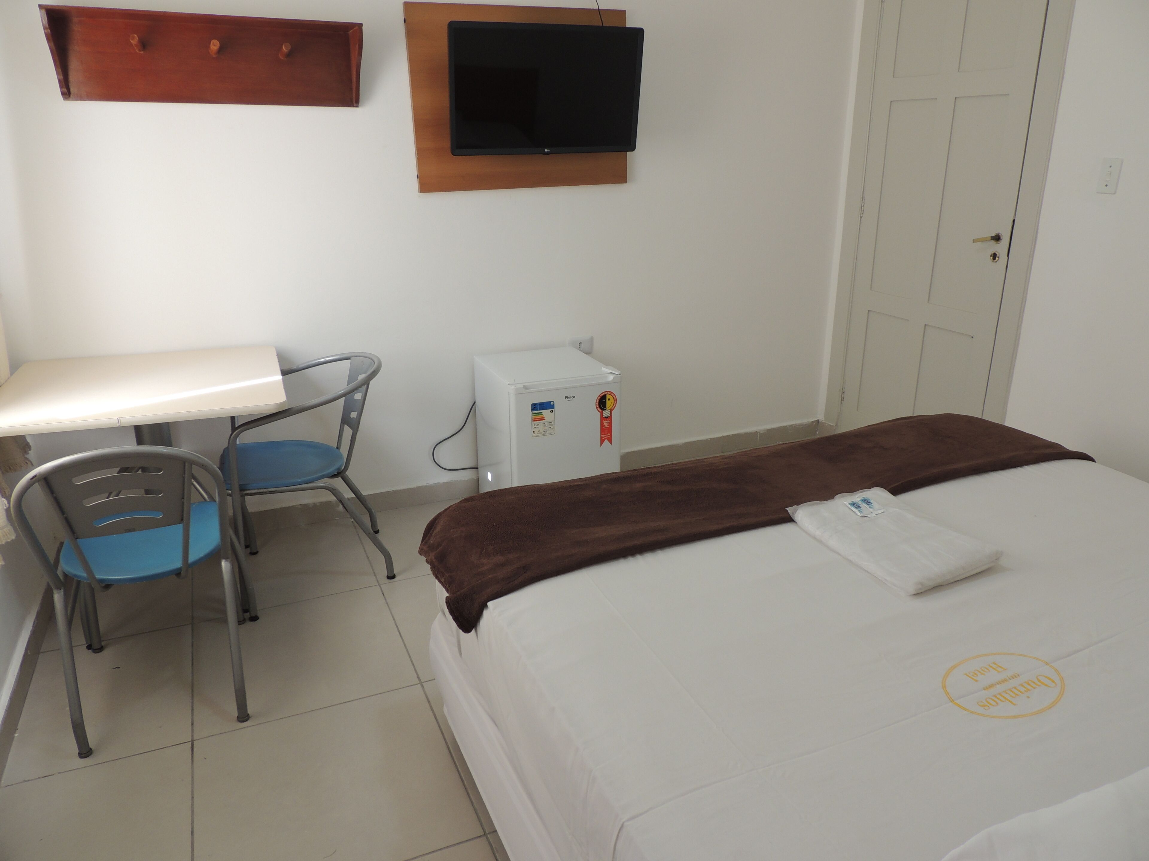 A hotel room with a bed, a desk, a chair, a television, and a refrigerator.