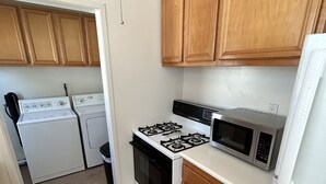Una cocina compacta con armarios de madera, una estufa a gas, un microondas, un refrigerador y una lavadora.