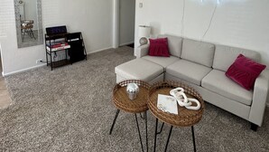 Un salón moderno con un sofá blanco, dos mesas redondas de mimbre, un letrero de neón y un espejo en la pared.