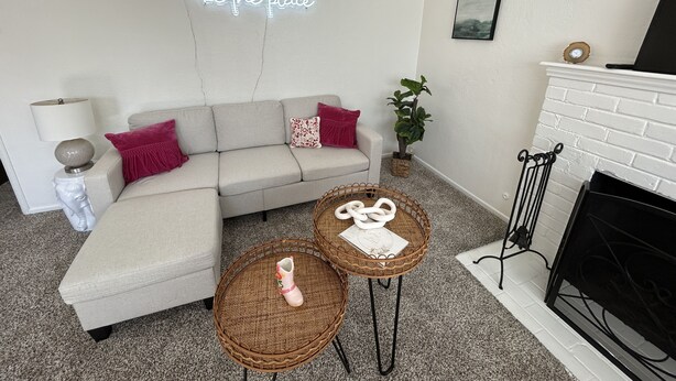 Una sala de estar moderna con un sofá blanco, un letrero de neón, una chimenea y una pequeña mesa con objetos decorativos.