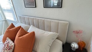 Un dormitorio ordenado con una cama, almohadas, una mesita de noche y dos cuadros en la pared.