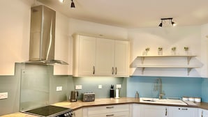 A modern kitchen with white cabinets, a stainless steel range hood, a built-in oven, a double sink, and a wooden countertop. - Smugglers View - Niton, sleeps 4 guests  in 2 bedrooms (Isle of Wight)