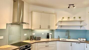 A modern kitchen with white cabinets, a stainless steel range hood, a built-in oven, a double sink, and a wooden countertop.