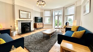 A living room with a fireplace, a television, a sofa, a coffee table, and a chandelier. - Smugglers View - Niton, sleeps 4 guests  in 2 bedrooms (Isle of Wight)