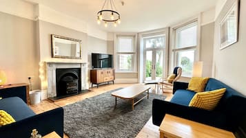 A living room with a fireplace, a television, a sofa, a coffee table, and a chandelier.