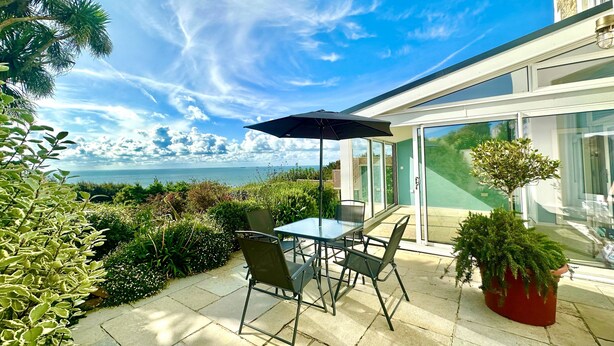 A patio with a table and chairs, a potted plant, and a view of the sea. - Smugglers View - Niton, sleeps 4 guests  in 2 bedrooms (Isle of Wight)