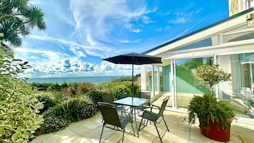 A patio with a table and chairs, a potted plant, and a view of the sea.