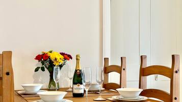 Une table à manger dressée avec des bols, des assiettes et des couverts blancs, une bouteille de champagne et un vase rempli de fleurs.