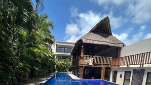 A swimming pool with a thatched-roof structure adjacent to it. - Bright Full Furnished 2 Bedrooms Waiting For You (Tulum)