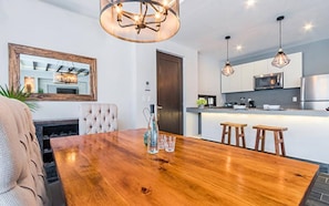 Uma cozinha moderna com eletrodomésticos de aço inoxidável, uma mesa de jantar de madeira com quatro banquetas e iluminação pendente.
