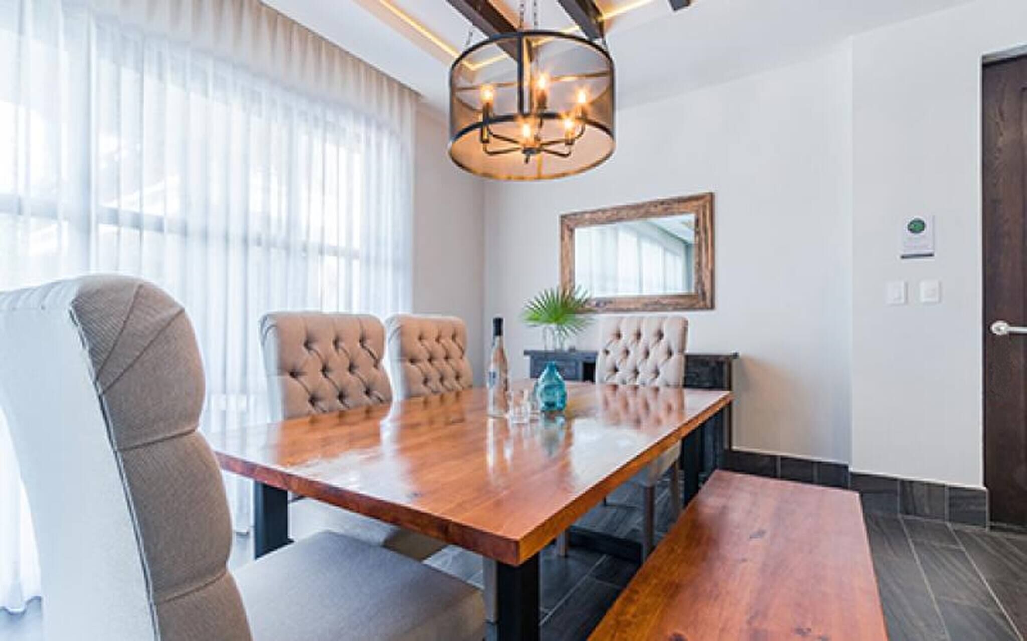 A modern dining area with a wooden table, cushioned chairs, and a chandelier.