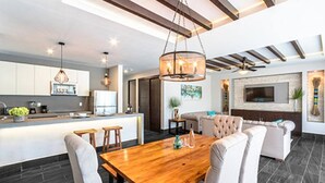 A modern kitchen with a central island, a dining area with a wooden table and chairs, and a living area with a sofa and a TV. - Bright Full Furnished 2 Bedrooms Waiting For You (Tulum)