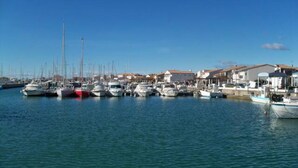 Un puerto deportivo con varias embarcaciones amarradas, un cielo azul despejado y edificios al fondo.