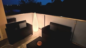 Una terraza en la azotea con dos sofás de mimbre negro, una mesita y una lámpara de pie grande.