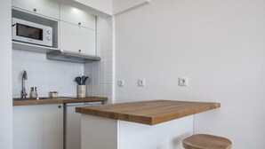 A kitchen with white cabinets, a microwave, a dishwasher, and a wooden countertop with two stools.