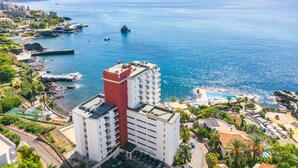 A coastal hotel with multiple floors, a swimming pool, and a view of the sea.