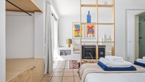 A modern bedroom with a bed, a wooden bench, a fireplace, and artwork on the wall.