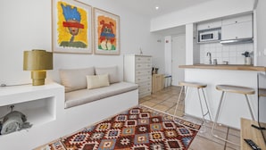 A modern kitchen with white cabinets, a microwave, and a sink. There is a bar stool area and a sofa with a patterned rug.