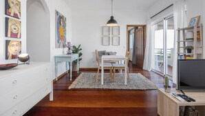 A modern living room with a dining area, wooden flooring, a white sofa, a coffee table, and a TV on a wooden stand. - Casa da Ângela - By Wehost (Funchal)