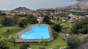 A swimming pool surrounded by greenery, with a view of a coastal town in the background. - Casa da Ângela - By Wehost (Funchal)